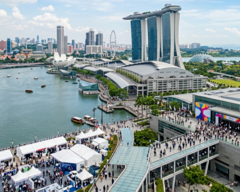 Singapore skyline overlooking Marina Bay with Marina Bay Sands, waterfront promenade, and a large public event near the convention centre.